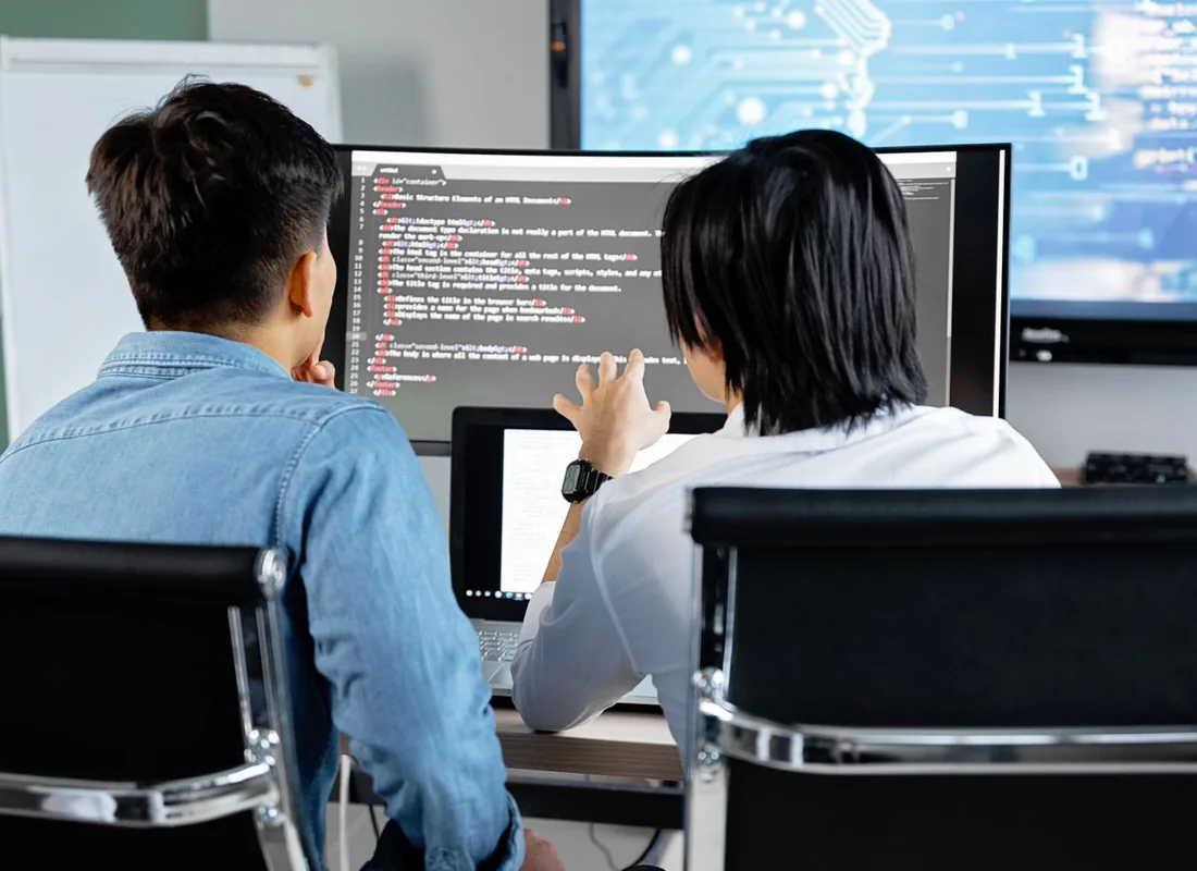 Deux ingénieurs IT examinent du code ensemble sur un écran en environnement de travail